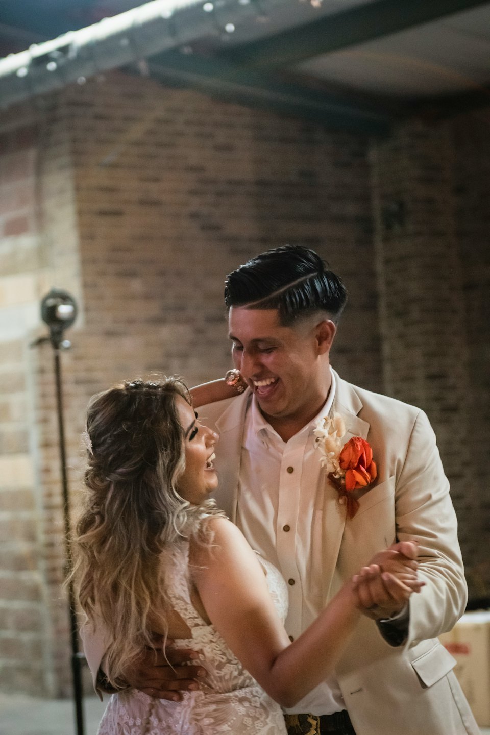 A bride and groom dance together in front of a brick wall.