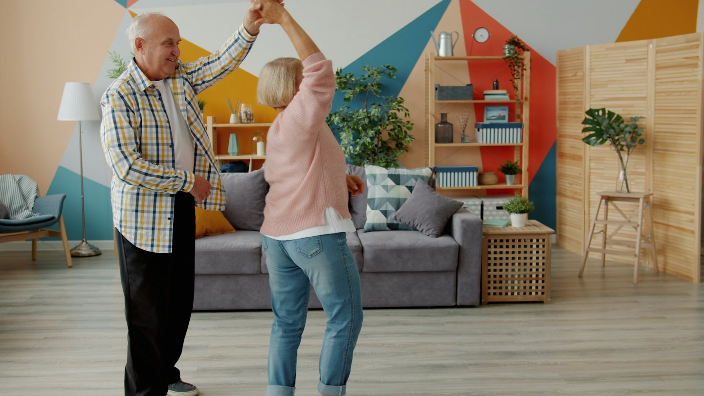 An older couple dances joyfully in a modern living room.
