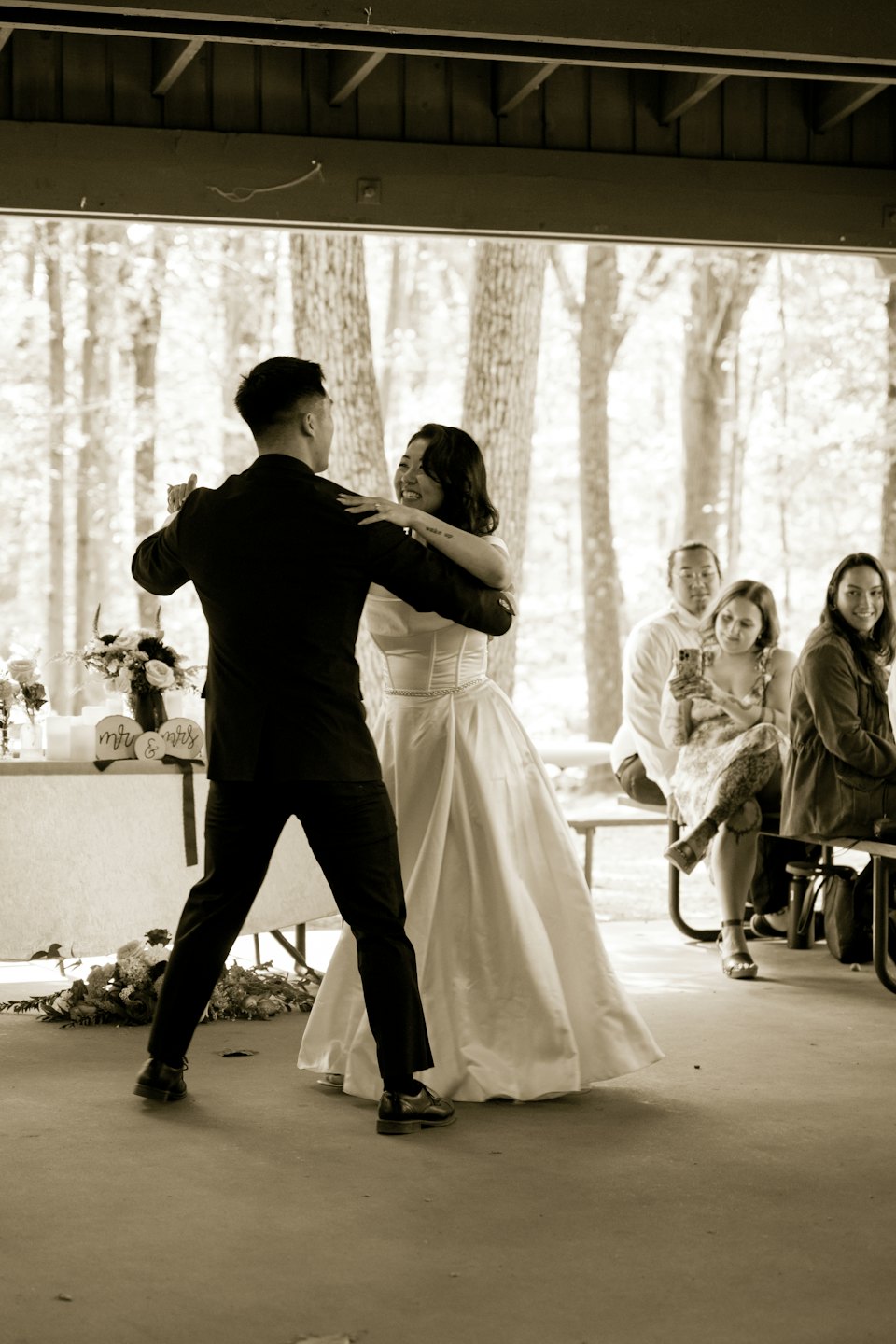 A couple dances happily under a wooden pavilion during their wedding.